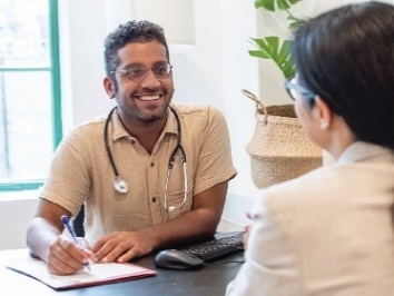 A doctor sitting across from a patient and writing on a document.