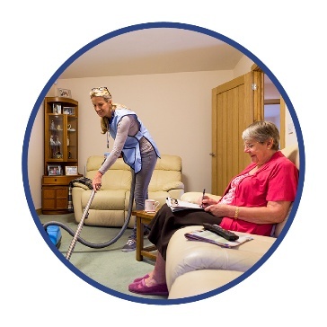 A support working vacuuming a living room for a person sitting on a couch.